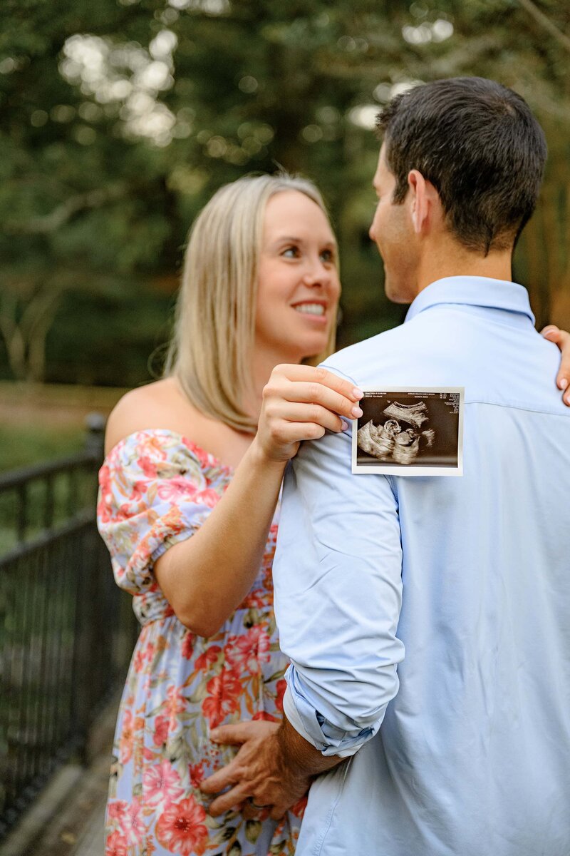 mother holds a ultrasound photo as her arms are around her husbands back