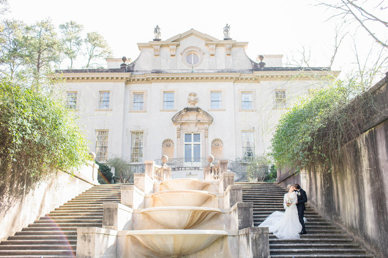 bride and groom standing on stairs in front of mansion