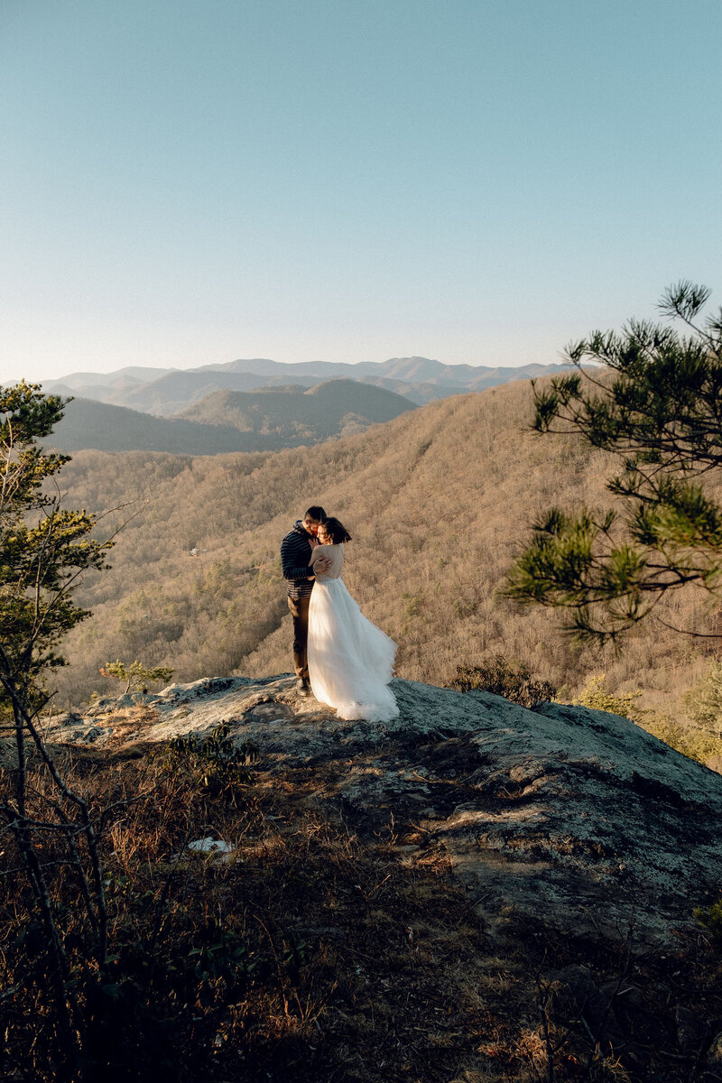 Eloping couple embraces each other on the edge of a mountain cliff