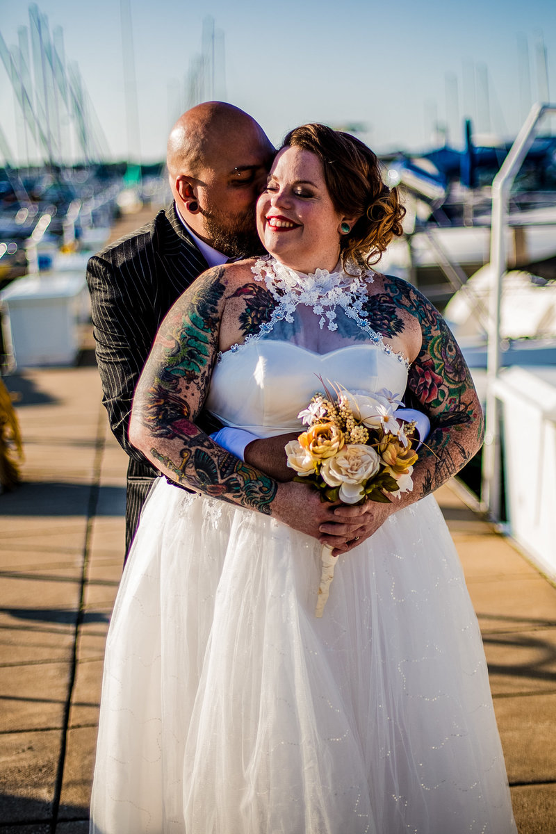 groom whispers in bride's ear as she smiles at the Erie Yacht Club