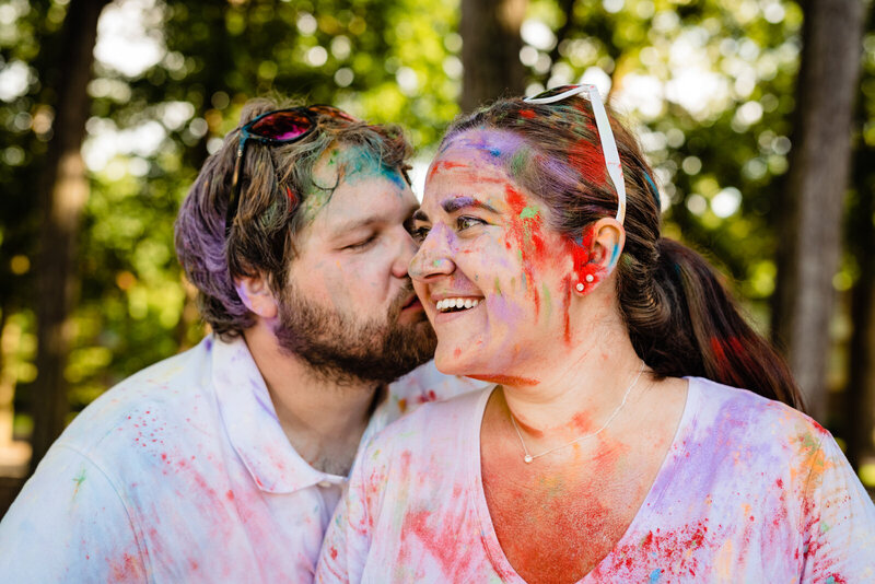 Couple covered in colorful powder smiles and kisses during their engagement photo session