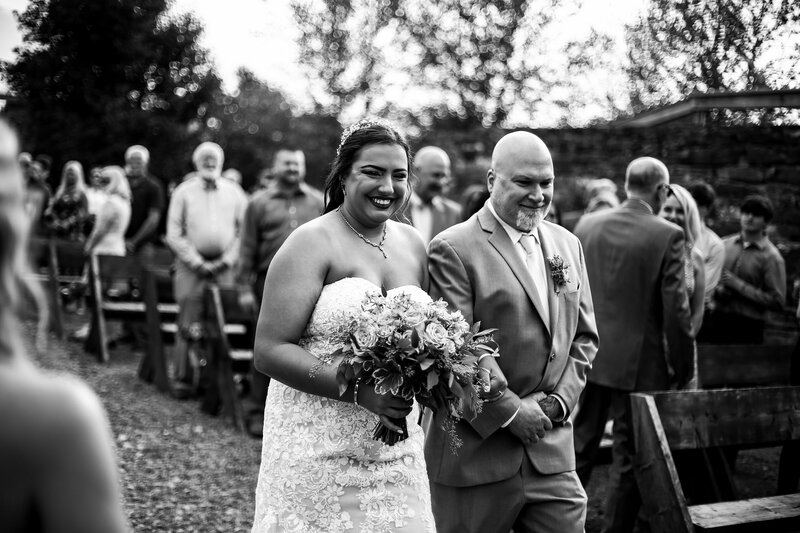 Bride smiles at groom while walking down the aisle at Port Farms