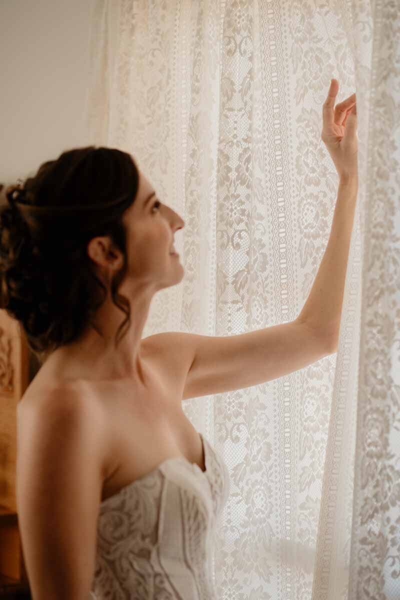 Bride touching the curtain while looking at the window light