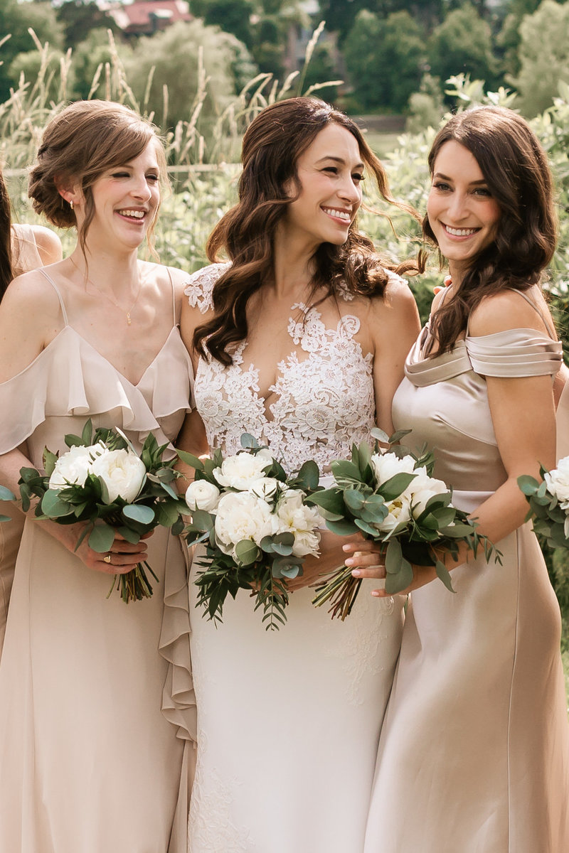 bride and bridesmaids smile as they pose with bouqets.