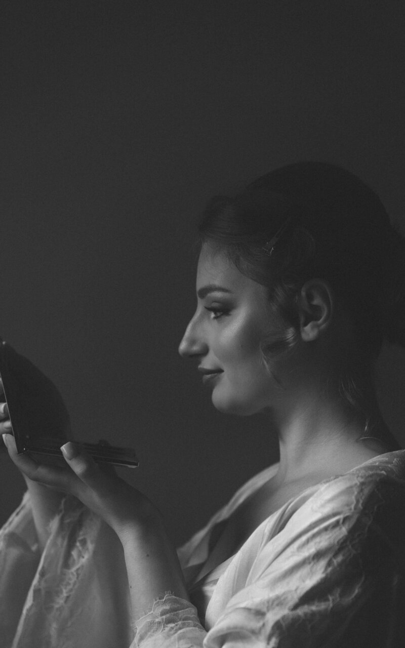 Black and white photo of the bride checking her reflection in the mirror, capturing a moment of anticipation and beauty as she prepares for her special day