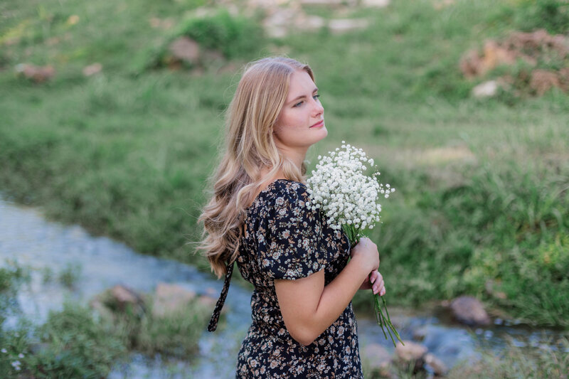 Blonde highschool senior who is homeschooled holds a bouquet of baby's breath in a black floral dress