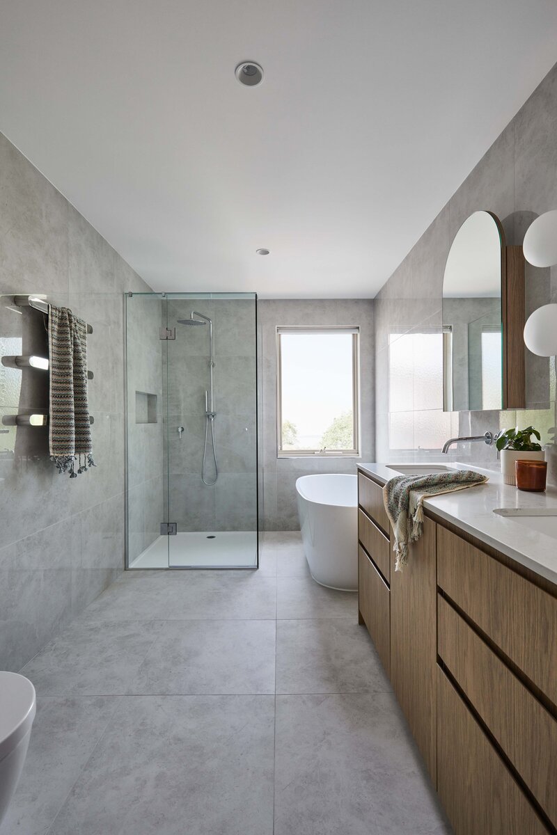 Contemporary bathroom with freestanding bath, glass shower, and timber double vanity | full service interior design for new builds and renovations