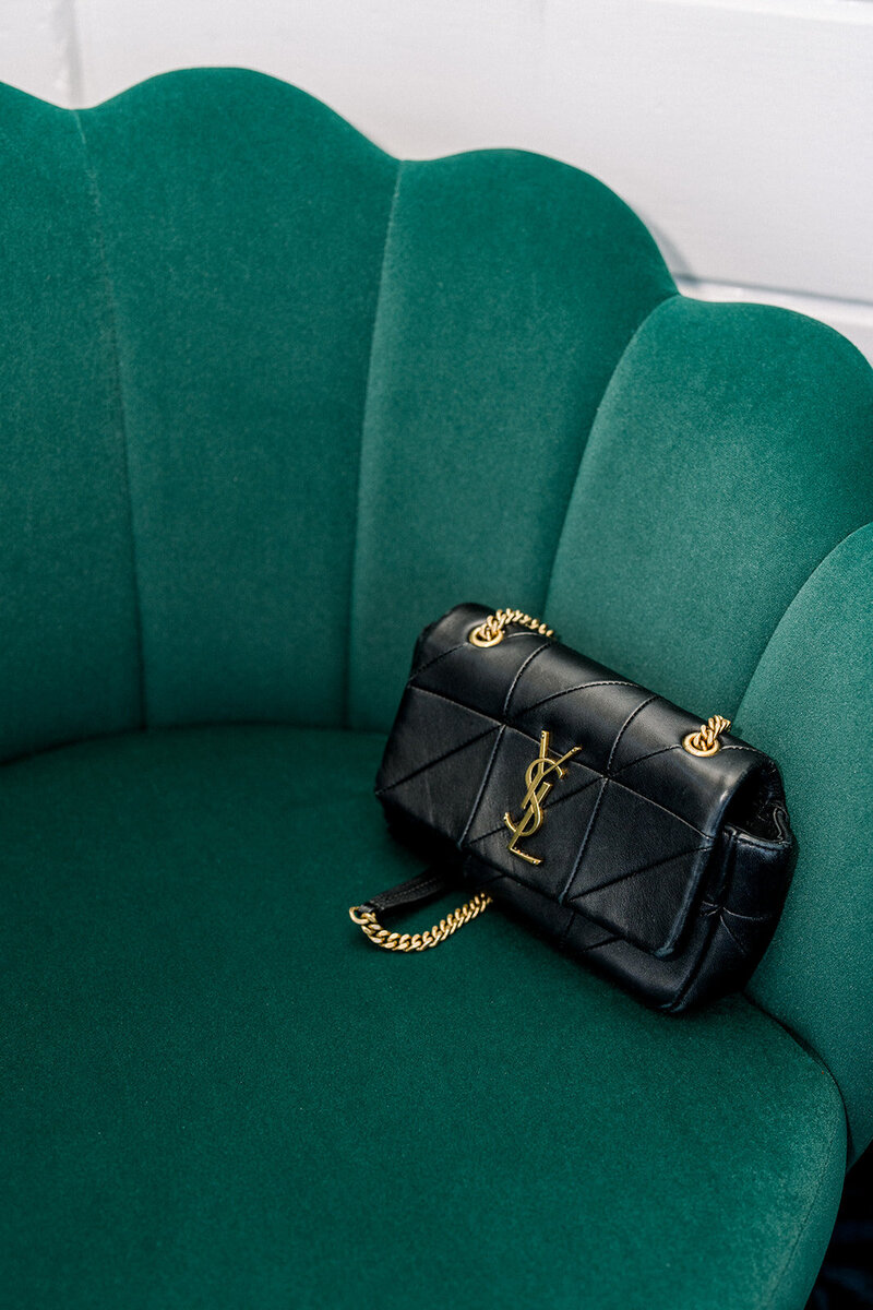 Elegant black Saint Laurent bag on a scalloped green velvet chair during wedding morning photography at a California Yacht Club.