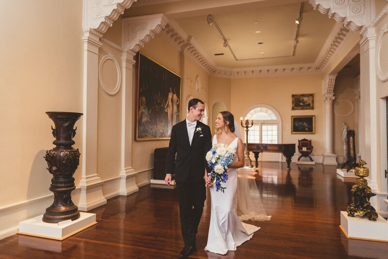 Groom and bride carrying a bouquet walking down the hall of an art museum