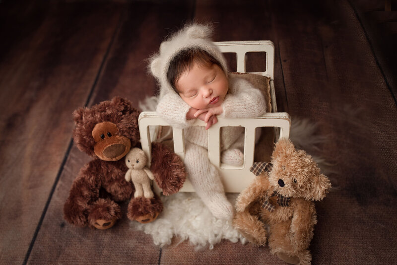 baby boy wearing a bear outfit posed on a mini bed with stuffed bears around