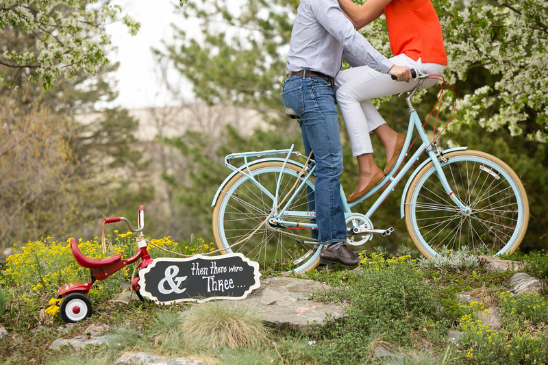 Newly expecting couple pose on a big with a tricycle in the foreground