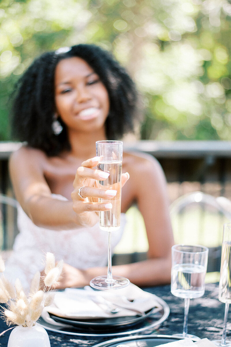 woman toasting her champange to the camer and smiling at a black themed minimalistic wedding table