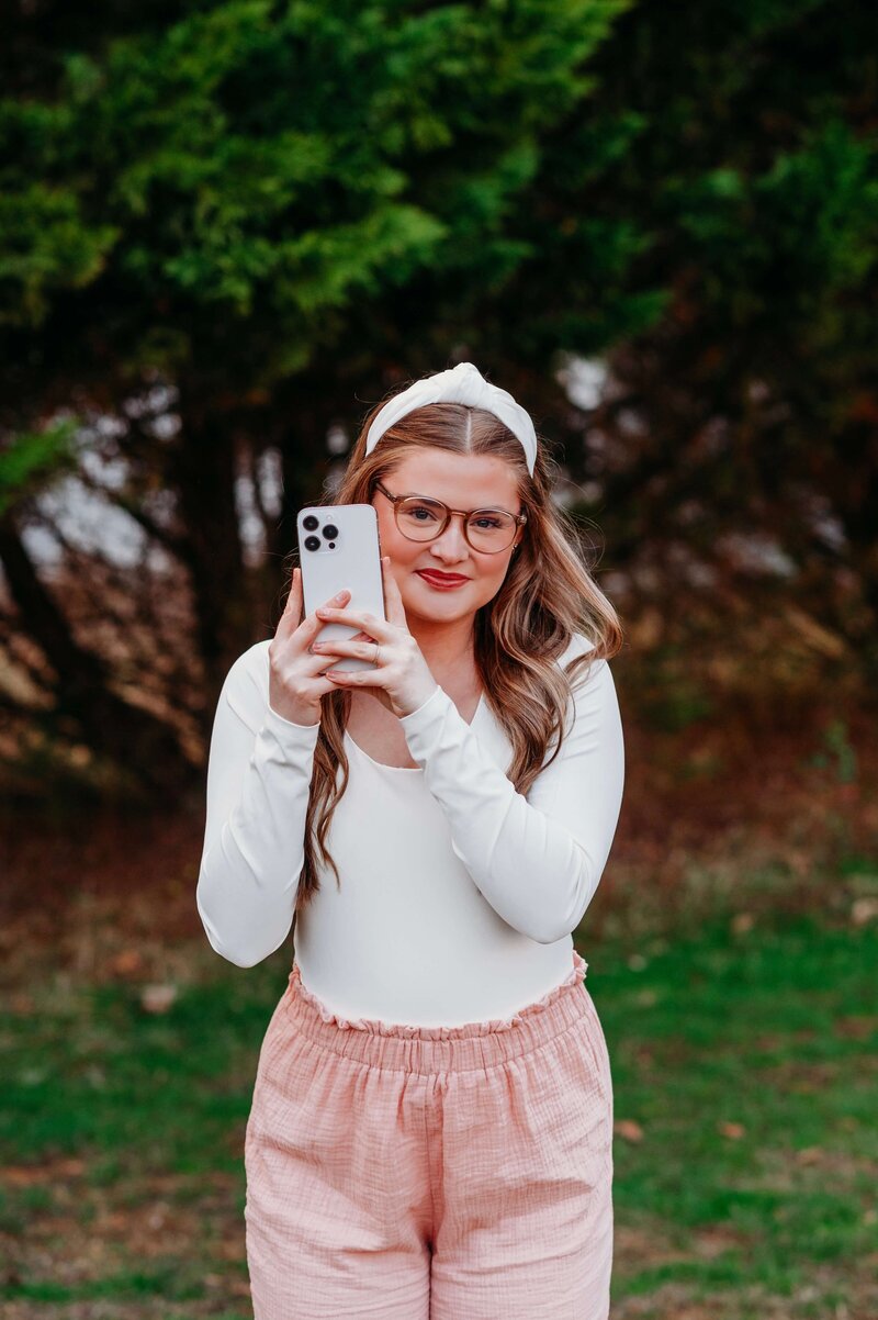photo of a young female adult holding an iphone and wearing glasses