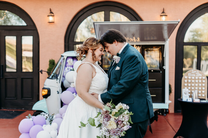 Married Couple posing in front of a bar truck with purple balloons