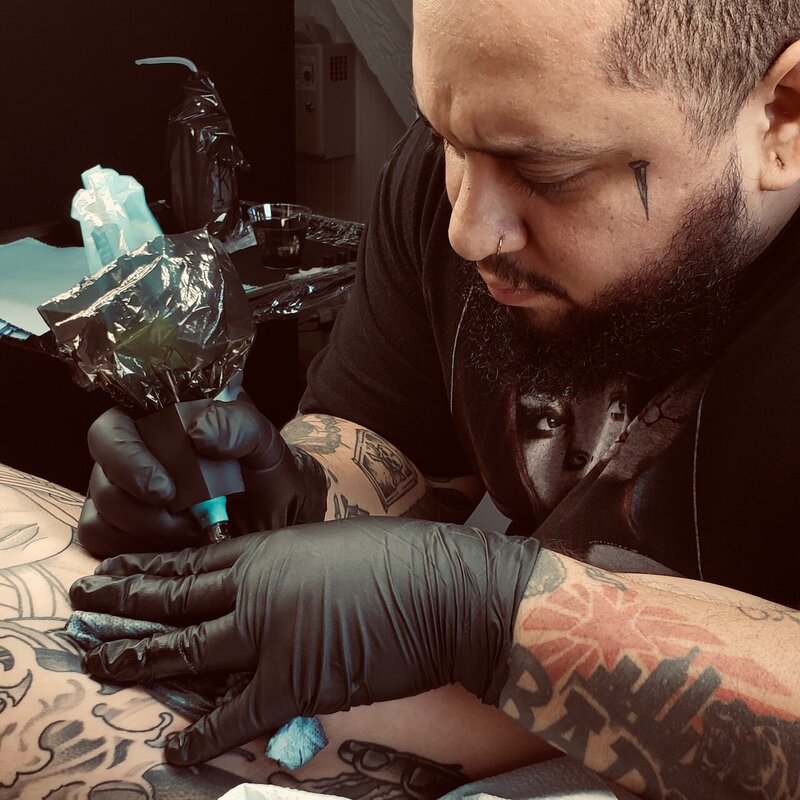 A man with hat and glasses tattooing.