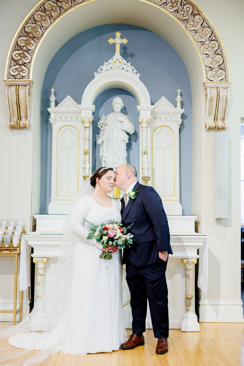 Bride and groom kiss in front of Saint Joseph statute before their ceremony