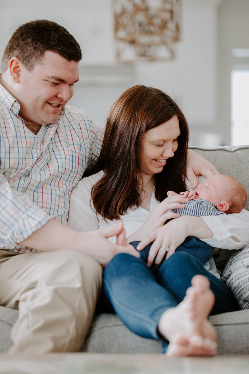 New parents smile as they hold their newborn son on the couch