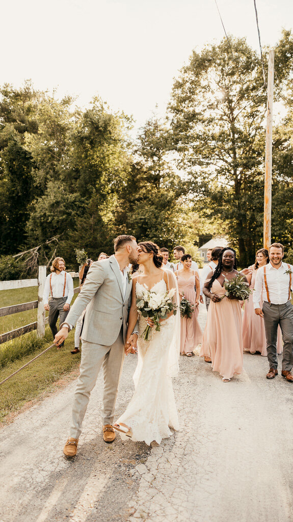The bride and groom lead the way, sharing a kiss, while their bridesmaids and groomsmen follow, adorned in beautiful attire.