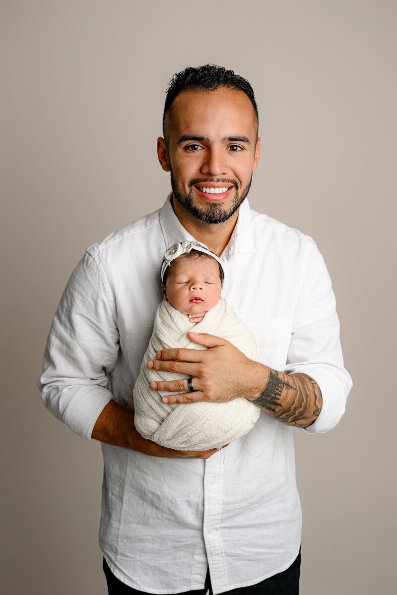 charlotte father holds his newborn daughter against his chest on a neutral set up 
