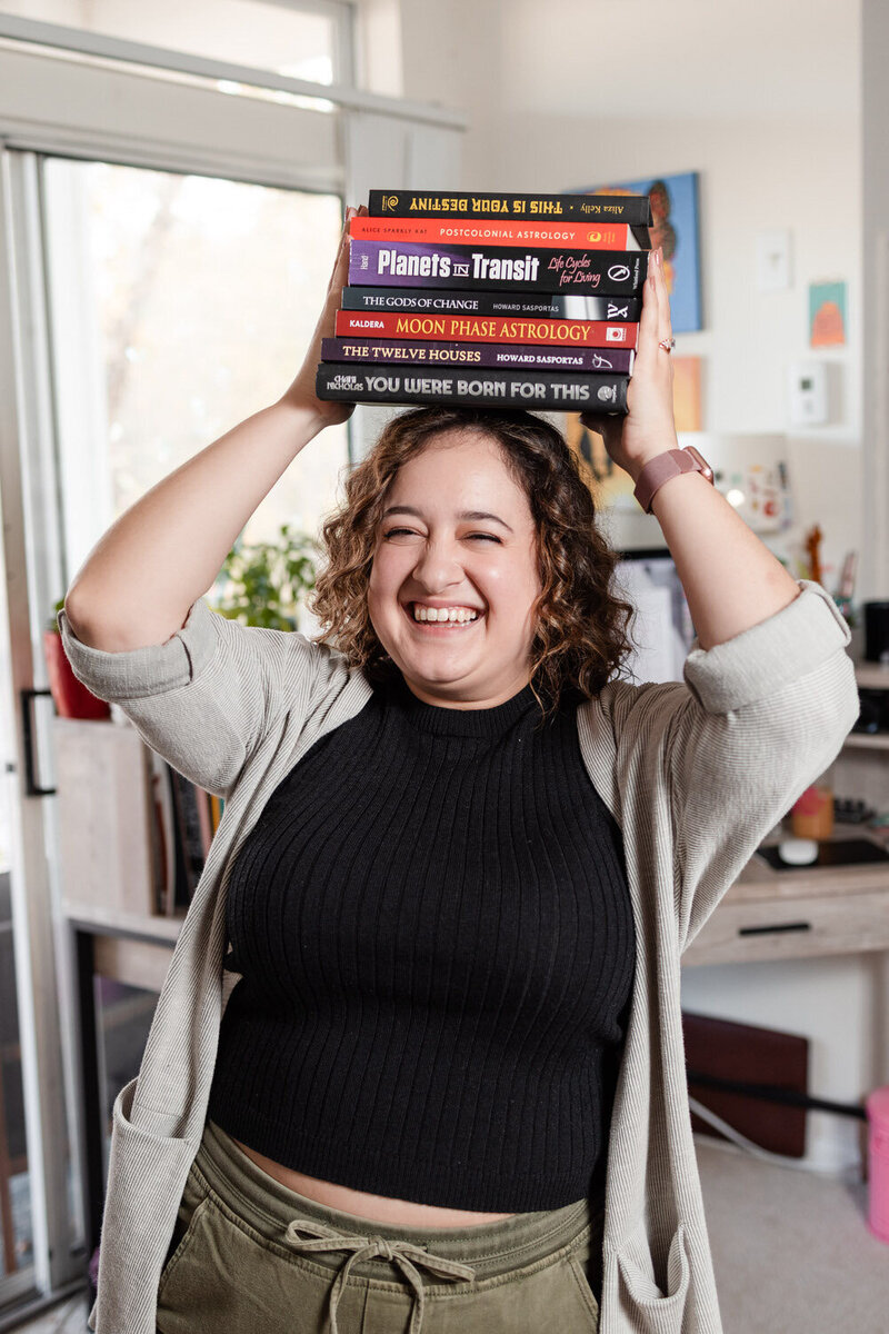 woman smiling and holding a stack of books on top of her head