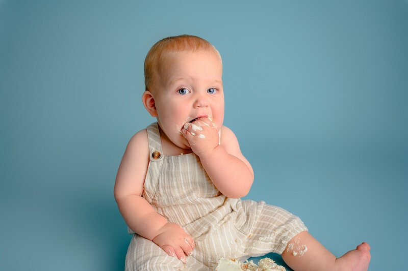 one year old boy sits taking a big bite of his smash cake