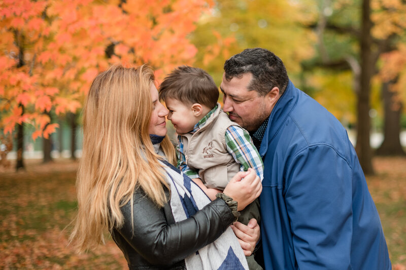 A family of three snuggle surrounded by a beautiful background of colourful fall leaves