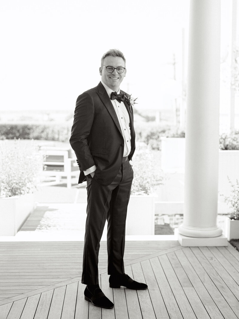 Black and white portrait of a groom standing outside in his tux