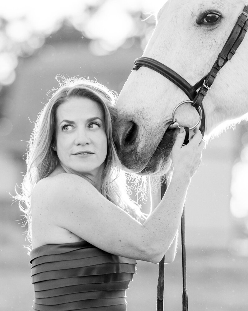 A close up image of a adult amateur hunter jumper resting her head on the nose of her grey senior gelding Ghost in a field at The Woodlands Equestrian in Edmond Oklahoma