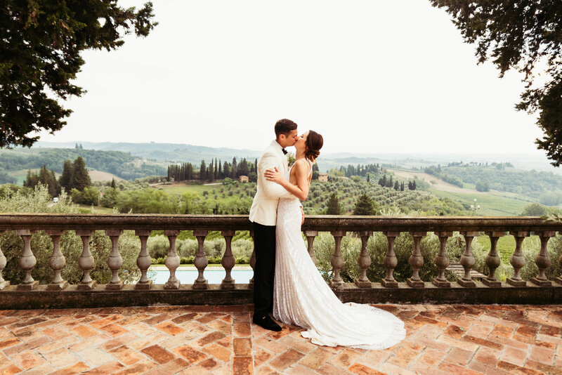 The bride and groom share a kiss, framed by the picturesque Tuscany hills, capturing the romance and beauty of their wedding day in this breathtaking photo