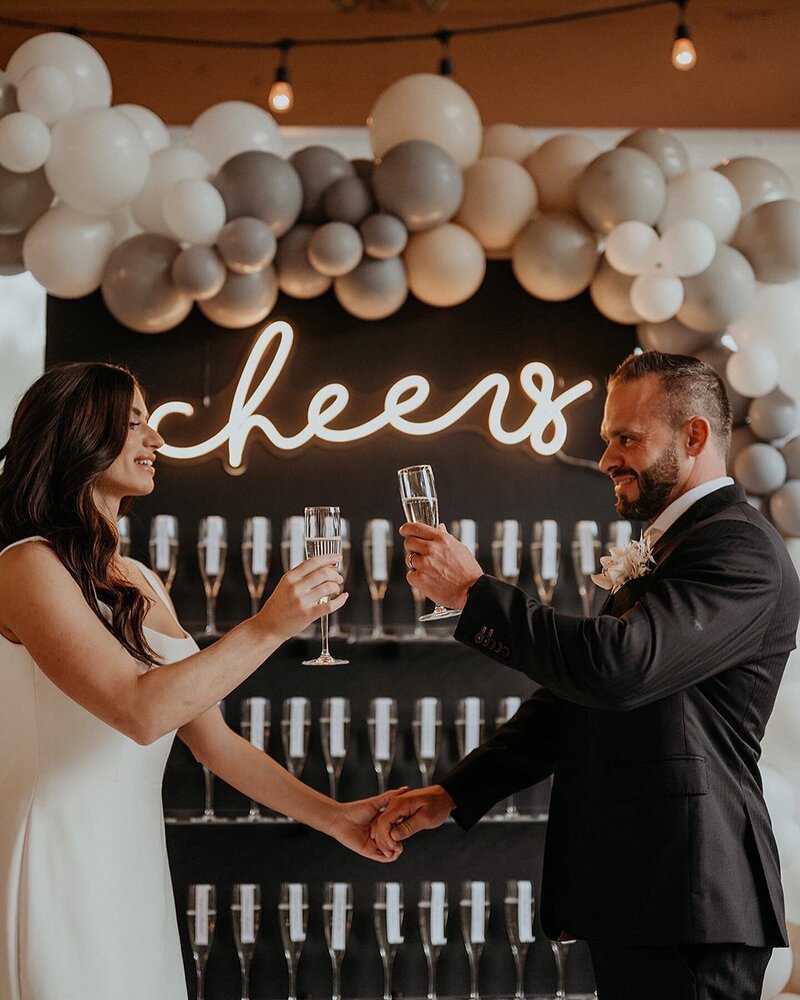 wedding couple cheersing in front of champagne wall design