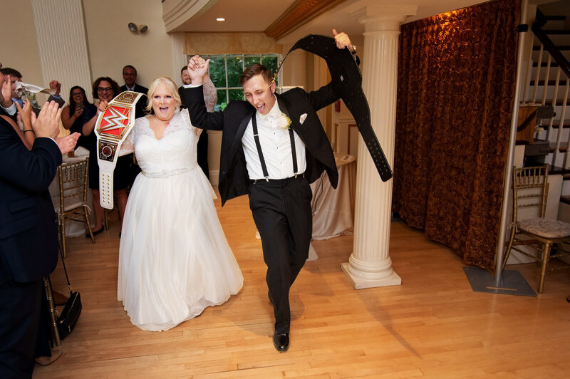 A newlywed couple walking into their reception with Wrestling belts in their hands