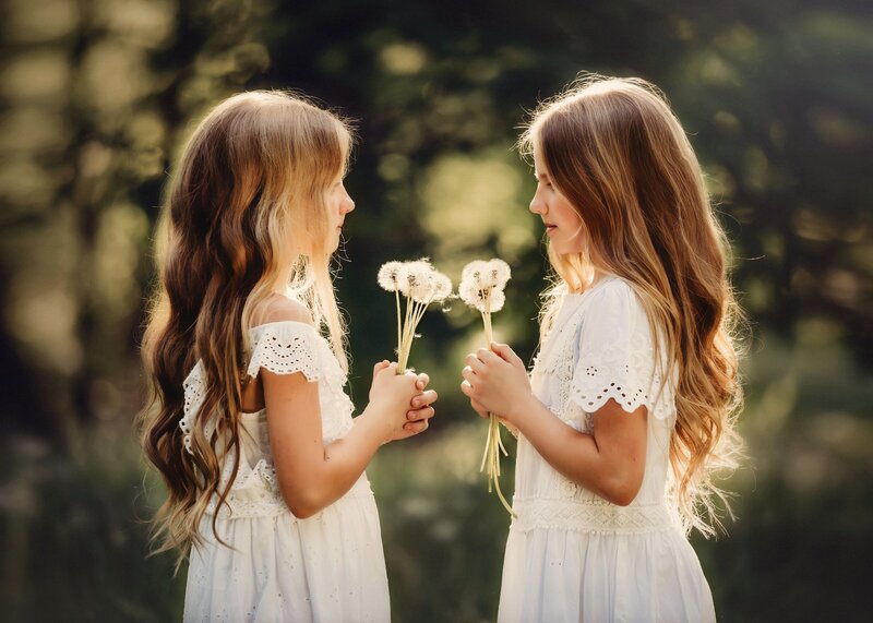 Sisters face each other in a field holding bouquets of dandelions