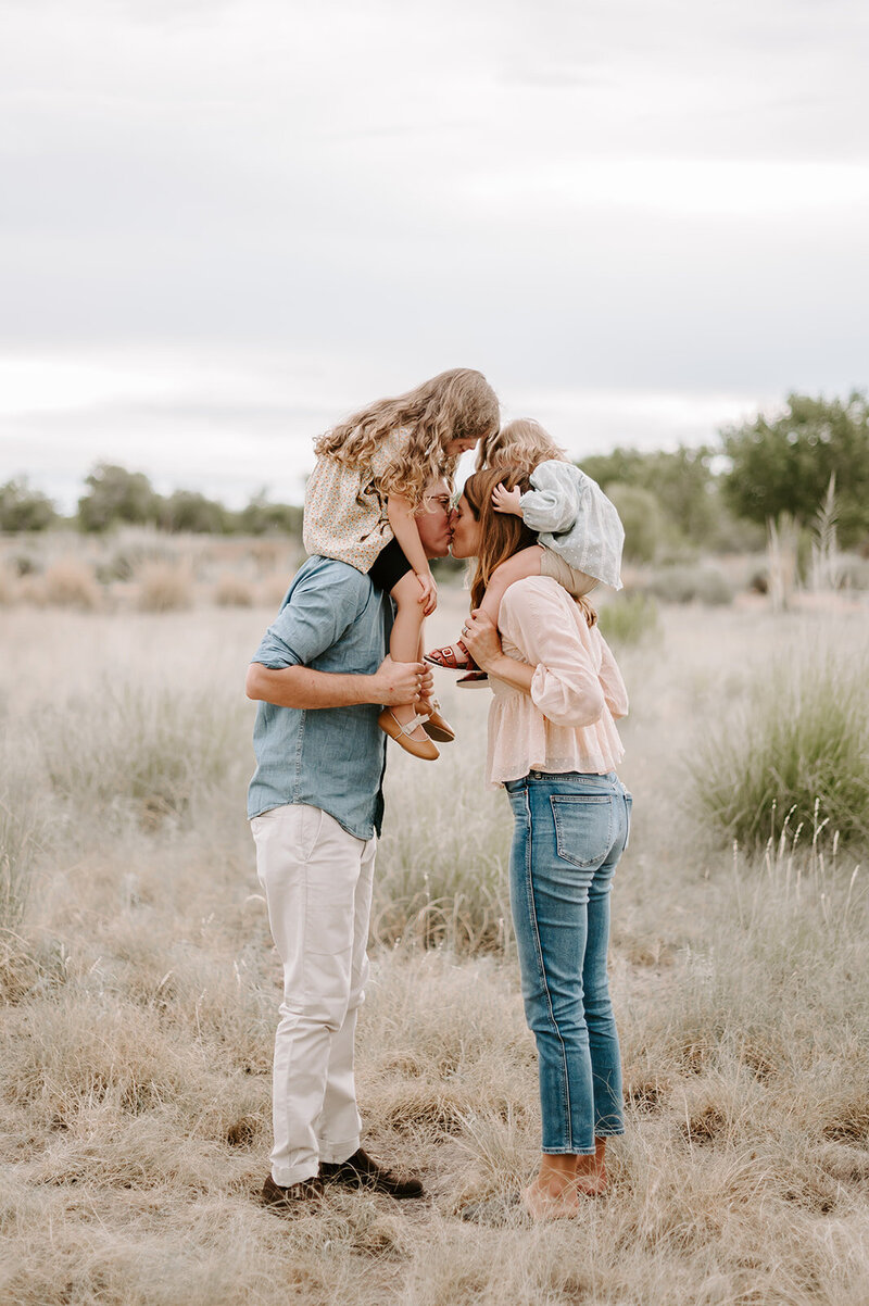 mom and dad holding kids kissing in a field