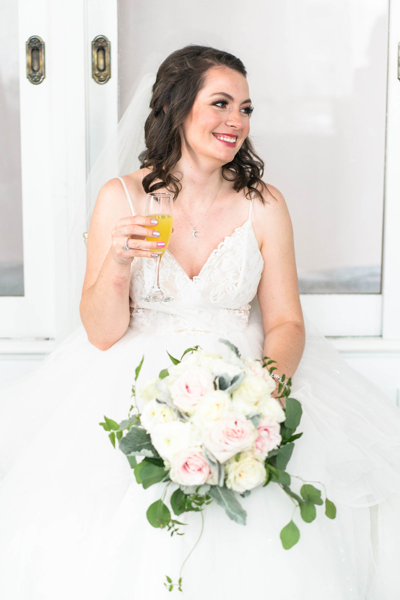 bride holing mimosa with white rose bouquet