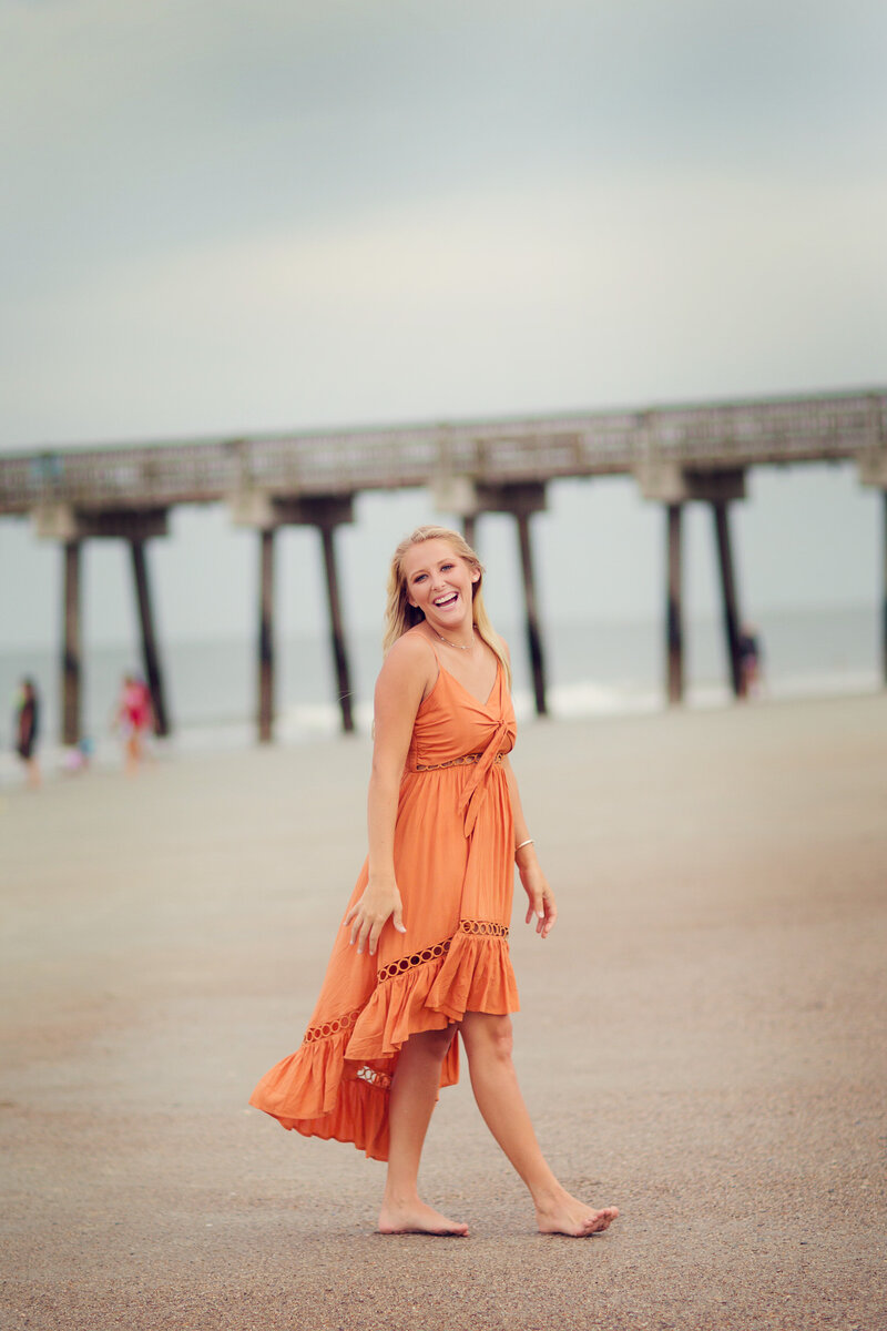 Senior girl on the beach at Tybee Island in a flowing orange summer dress.