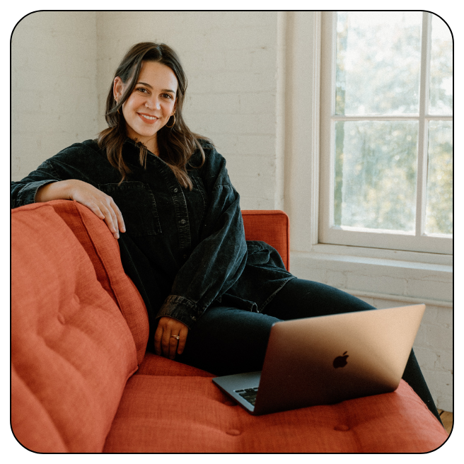 Brand designer Emma Leigh Studios portrait sitting on red sofa.