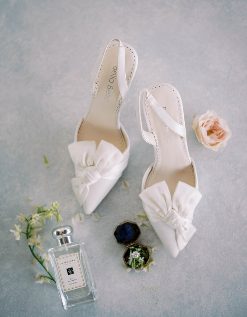 wedding shoes, perfumes and florals laid out to create a flatlay