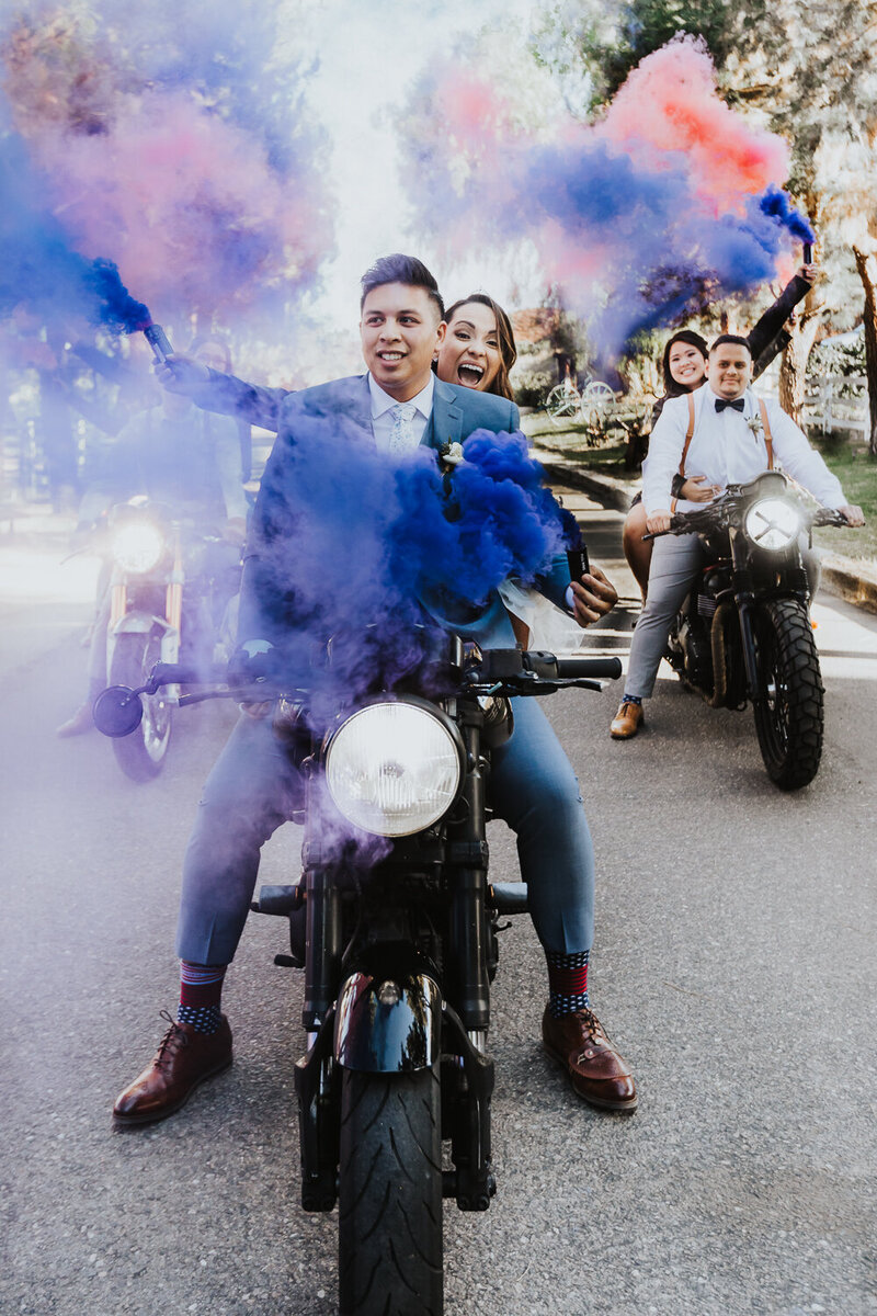 Elopement Photographer, bride and groom sit on motorcycle with smoke canister releasing colored smoke around them