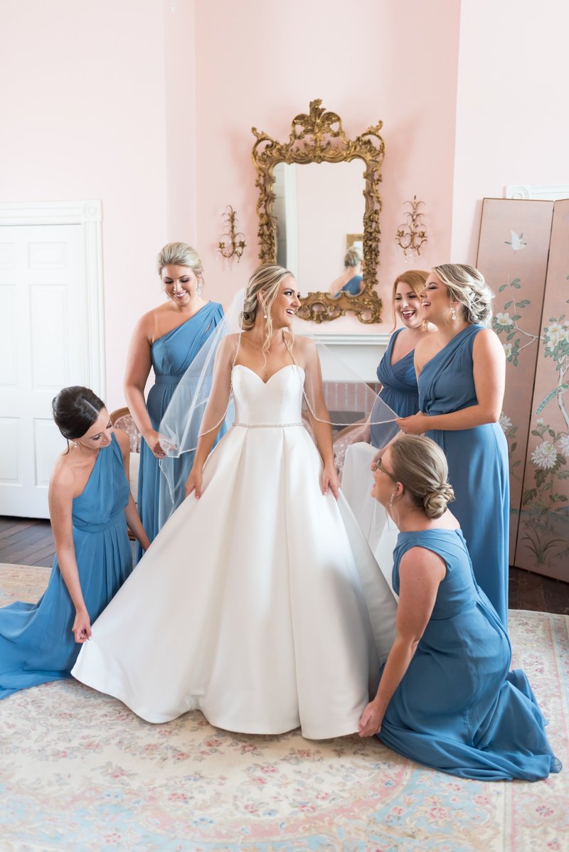 Bride in wedding gown with bridesmaids in blue dresses surrounding her at Ravenswood Mansion