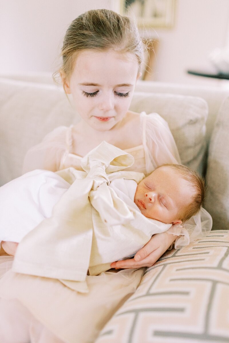 Big sister holding new baby on couch