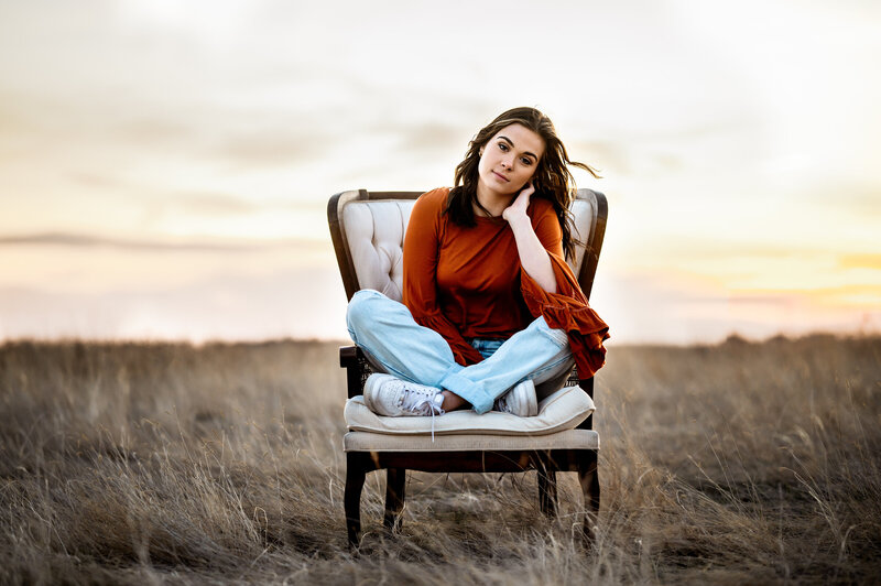 Girl sits in vintage wingback chair in field