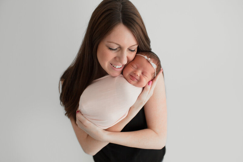 tiny newborn baby girl smiling while sleeping with mom smiling holding in arms