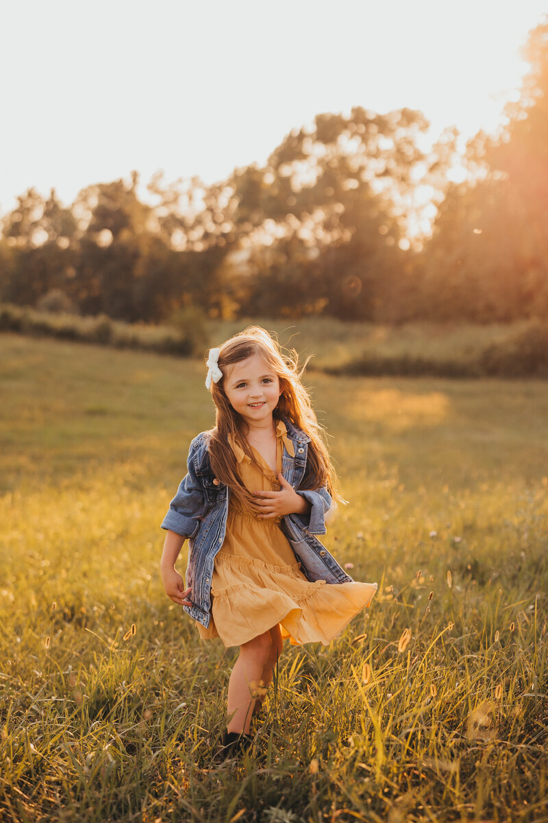 Family golden hour portrait of young girl walking through field of grass