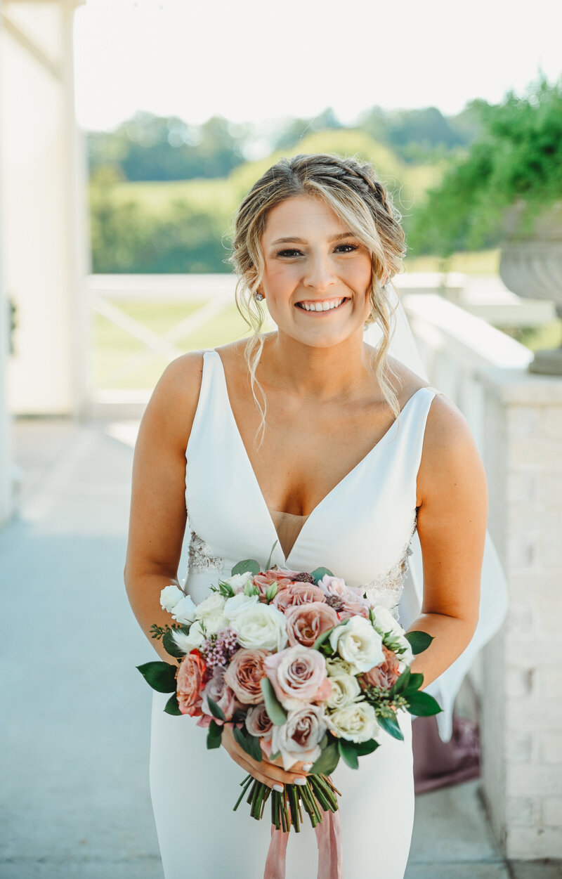 Bride outside of White Dove Barn holding a rose filled bouquet smiling at the camera