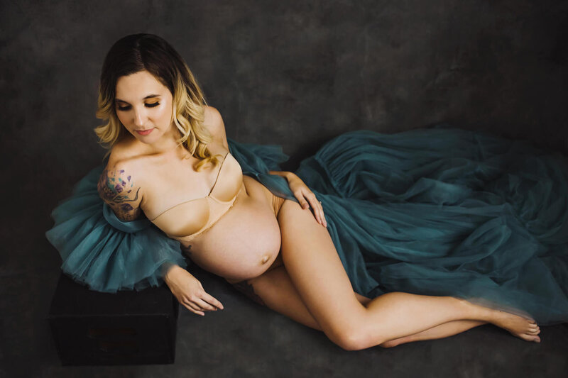 beautiful pregnant mom laying down wearing nude lingerie and a green tulle robe