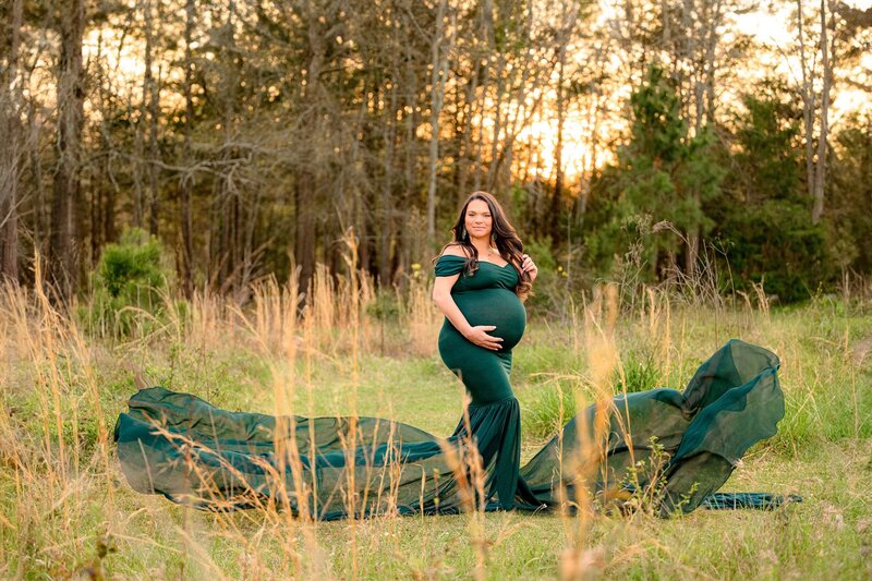 The forest green train on this maternity dress flows on both sides of mom as she's dramatically posed in a field
