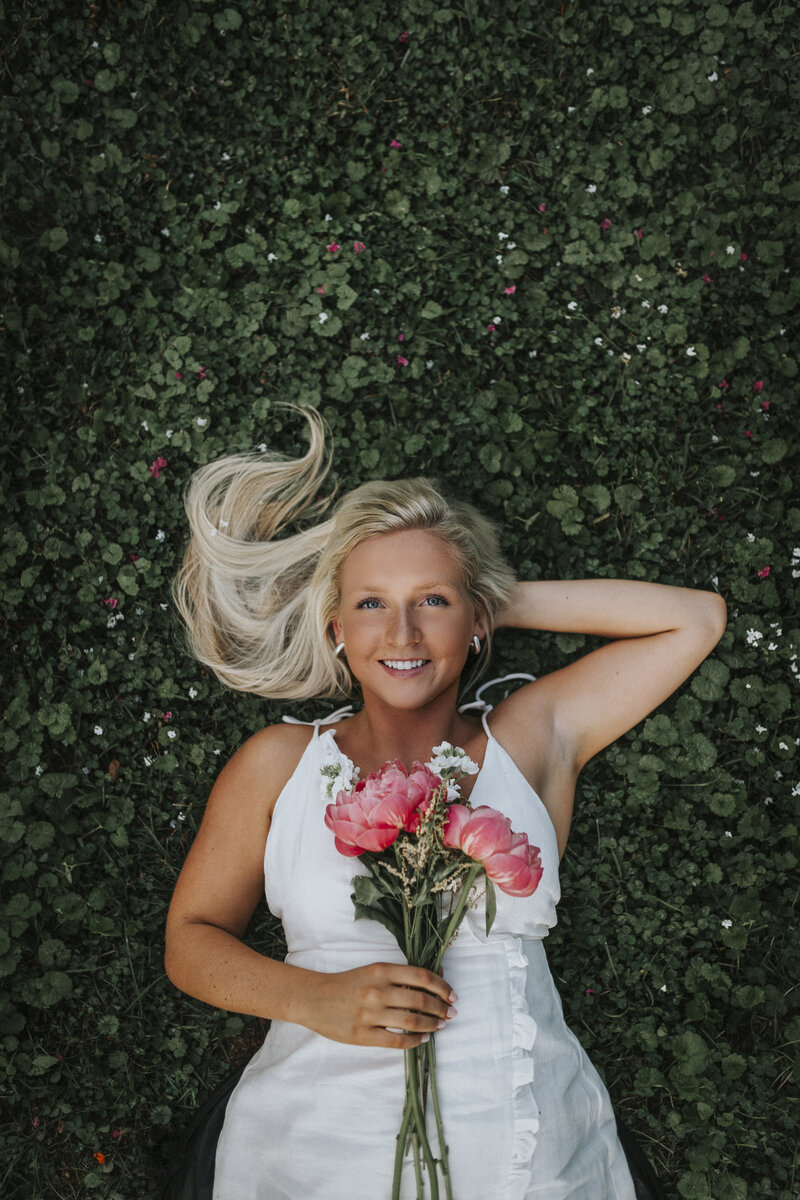 Unique, creative, and fun senior portrait of a girl holding flowers, laying in the grass