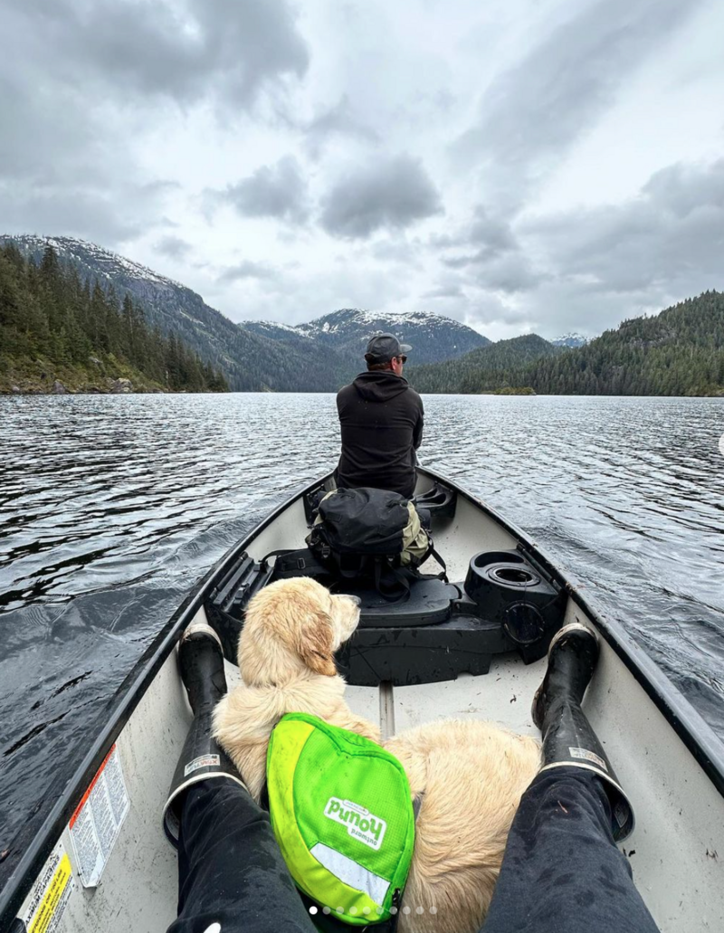 A couple riding a canoe on beautiful mountain lake  with dog calmly laying down in canoe | Cornerstone Dog Training