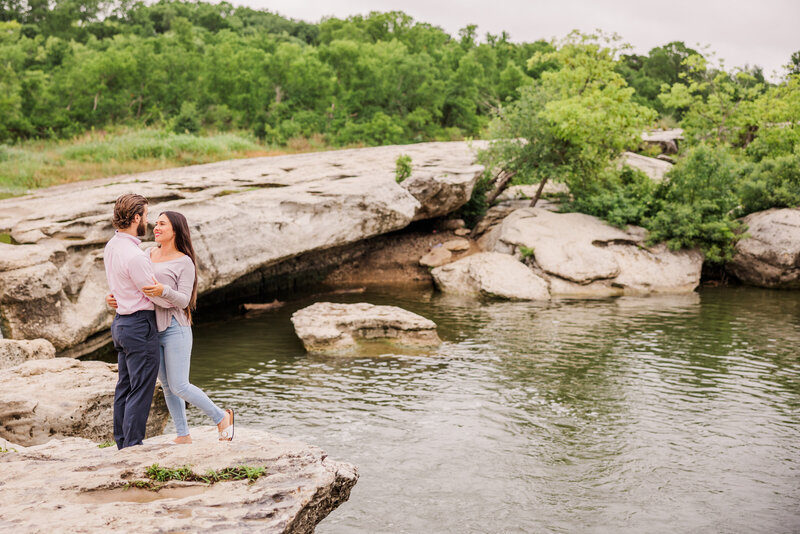 Couple embrace along the water during their engagement session at Mckinney Falls State Park in Austin, Texas.Photo taken by Austin Engagement Photographers, Joanna & Brett Photography