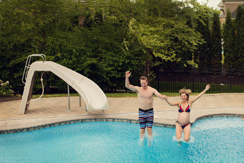 Husband and wife jump into their pool holding hands for a maternity session.